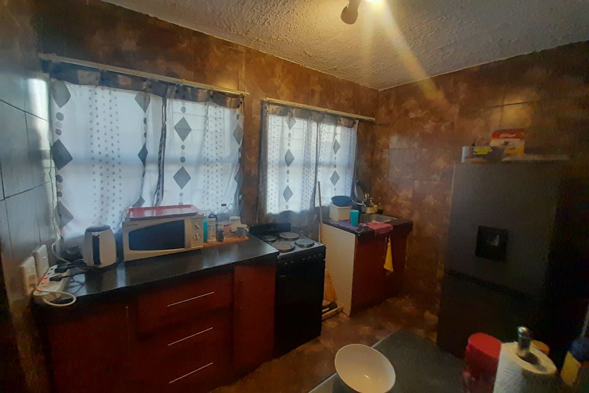 A compact kitchen featuring dated wall tiling, built-in cabinetry, and a functional stove, offering potential for a modern renovation.