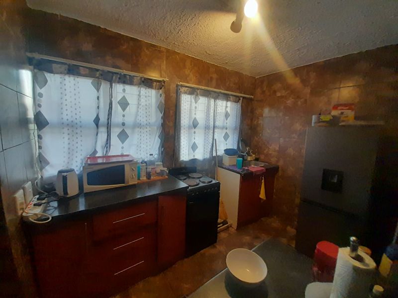 A compact kitchen featuring dated wall tiling, built-in cabinetry, and a functional stove, offering potential for a modern renovation.