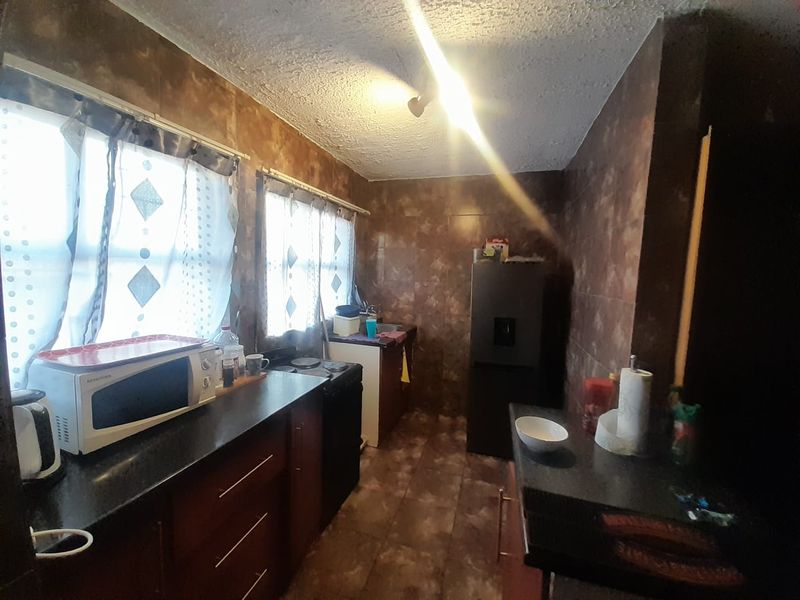 A compact kitchen featuring dark cabinetry, tiled wall finishes, and laminate countertops, currently in need of modernization to improve functionality and aesthetic appeal.