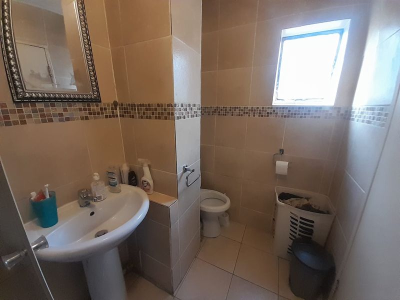 A functional bathroom featuring a pedestal washbasin, toilet, and neutral wall tiles with a decorative mosaic border.