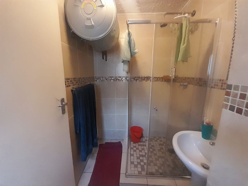 Compact bathroom featuring a glass shower enclosure, pedestal basin, and wall-mounted electric water heater with tiled finishes.