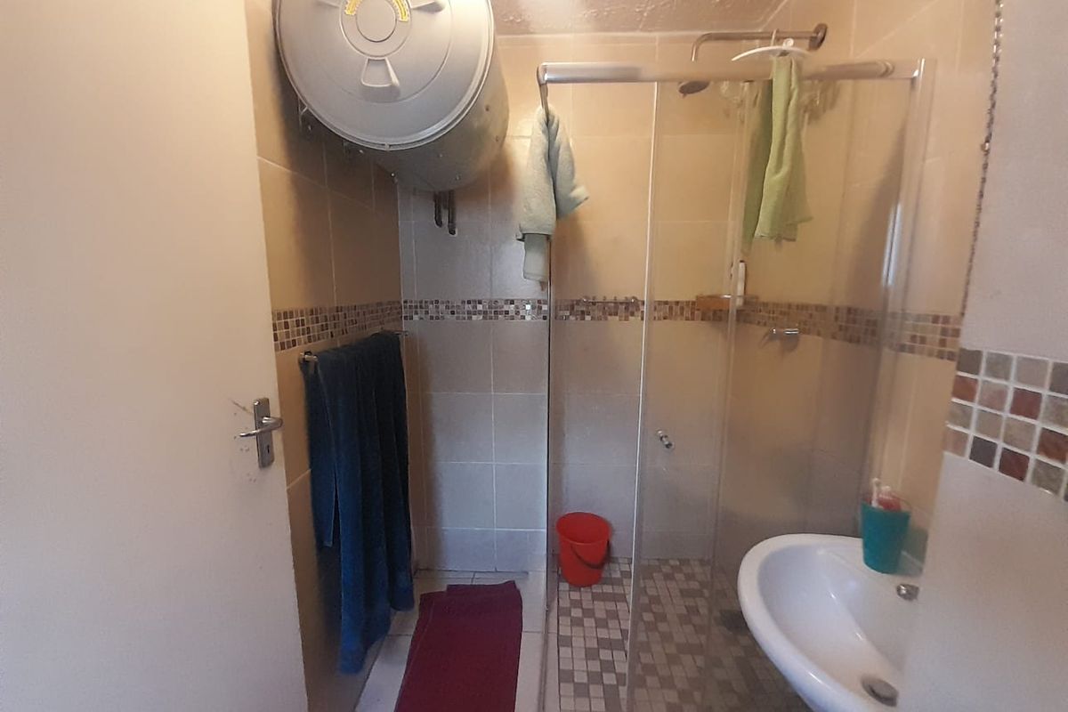 A compact bathroom featuring a shower enclosure, pedestal basin, and wall-mounted electric geyser with tiled finishes.