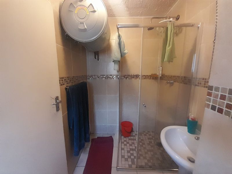 A compact bathroom featuring a shower enclosure, pedestal basin, and wall-mounted electric geyser with tiled finishes.