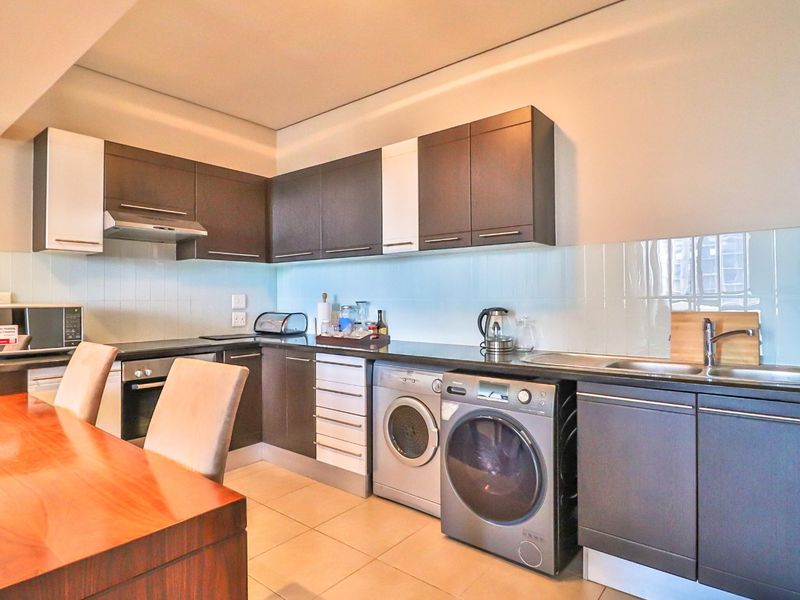 Modern kitchen featuring dark cabinetry, integrated appliances, tiled splashback, and tiled flooring, offering a functional and contemporary cooking space.