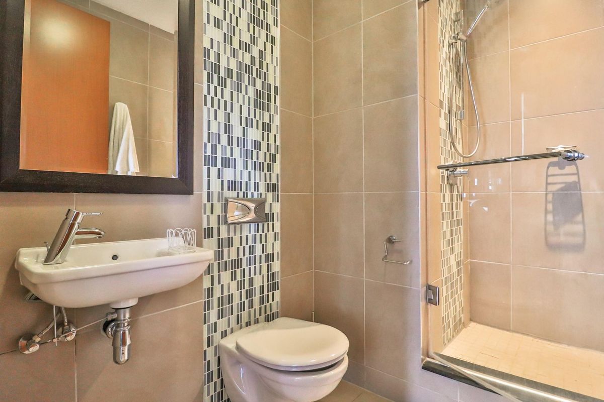 Modern bathroom featuring a wall-hung toilet, wall-mounted basin, and a glass-enclosed shower with decorative mosaic tile accents.