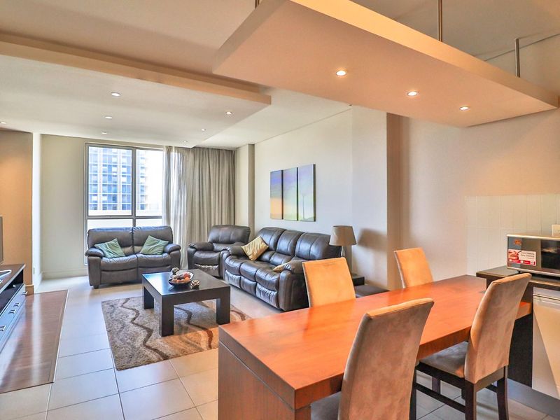 An open-plan living and dining area featuring tiled floors, recessed ceiling lighting, and a suspended bulkhead, creating a bright and functional living space.