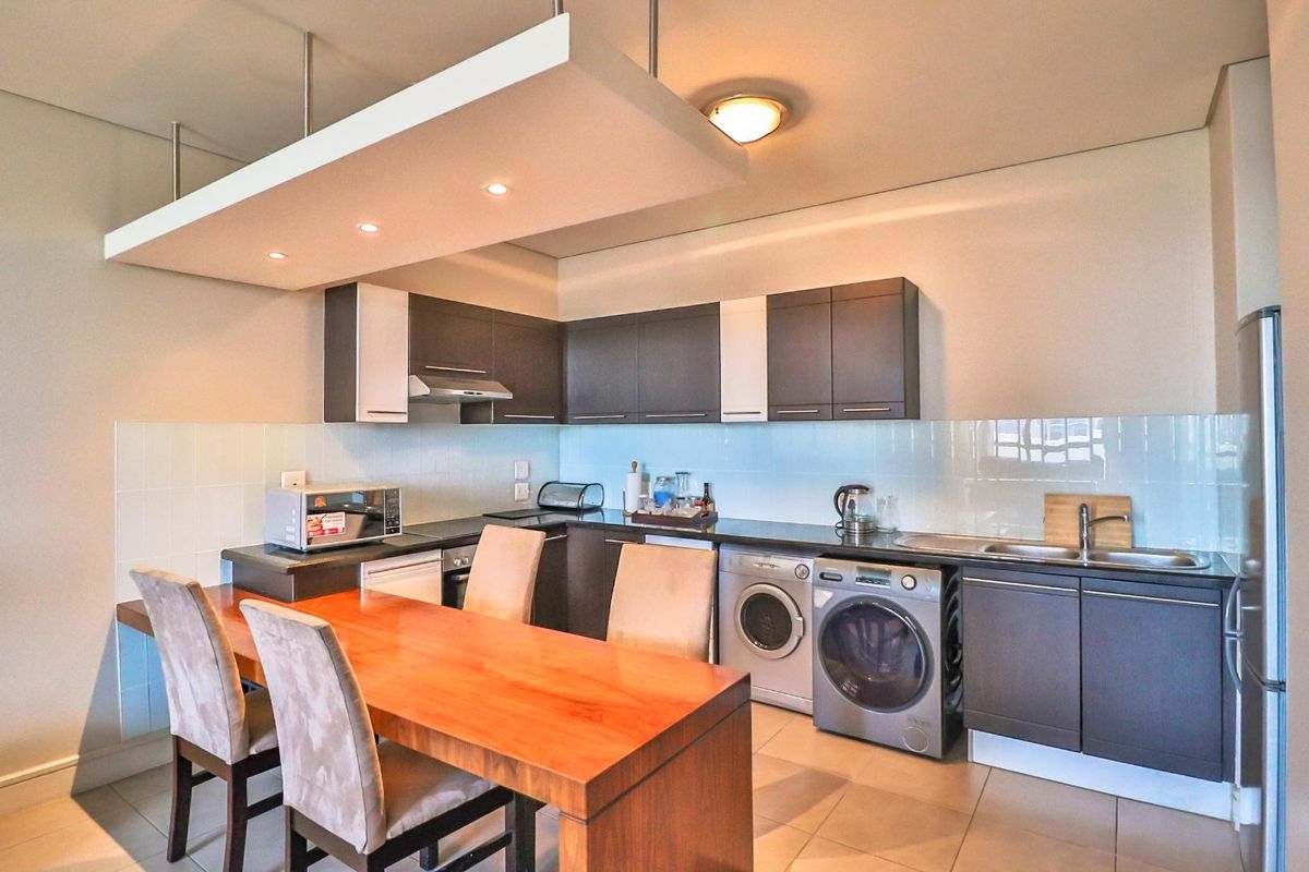 Modern kitchen featuring dark cabinetry, integrated appliances, tiled backsplash, and a suspended bulkhead with recessed lighting, providing a functional and contemporary cooking space.