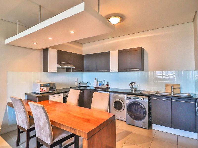 Modern kitchen featuring dark cabinetry, integrated appliances, tiled backsplash, and a suspended bulkhead with recessed lighting, providing a functional and contemporary cooking space.
