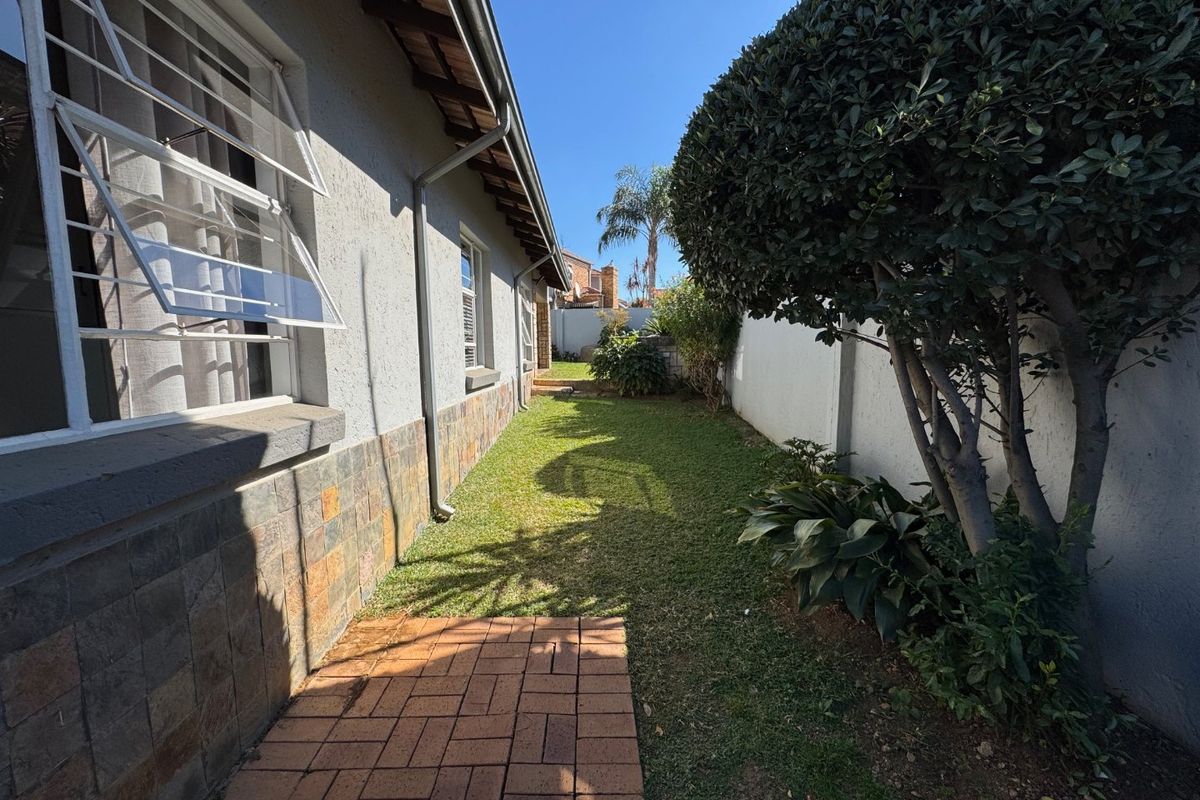 A side garden area featuring a paved walkway, manicured lawn, and perimeter boundary wall, providing a private outdoor space along the townhouse exterior.