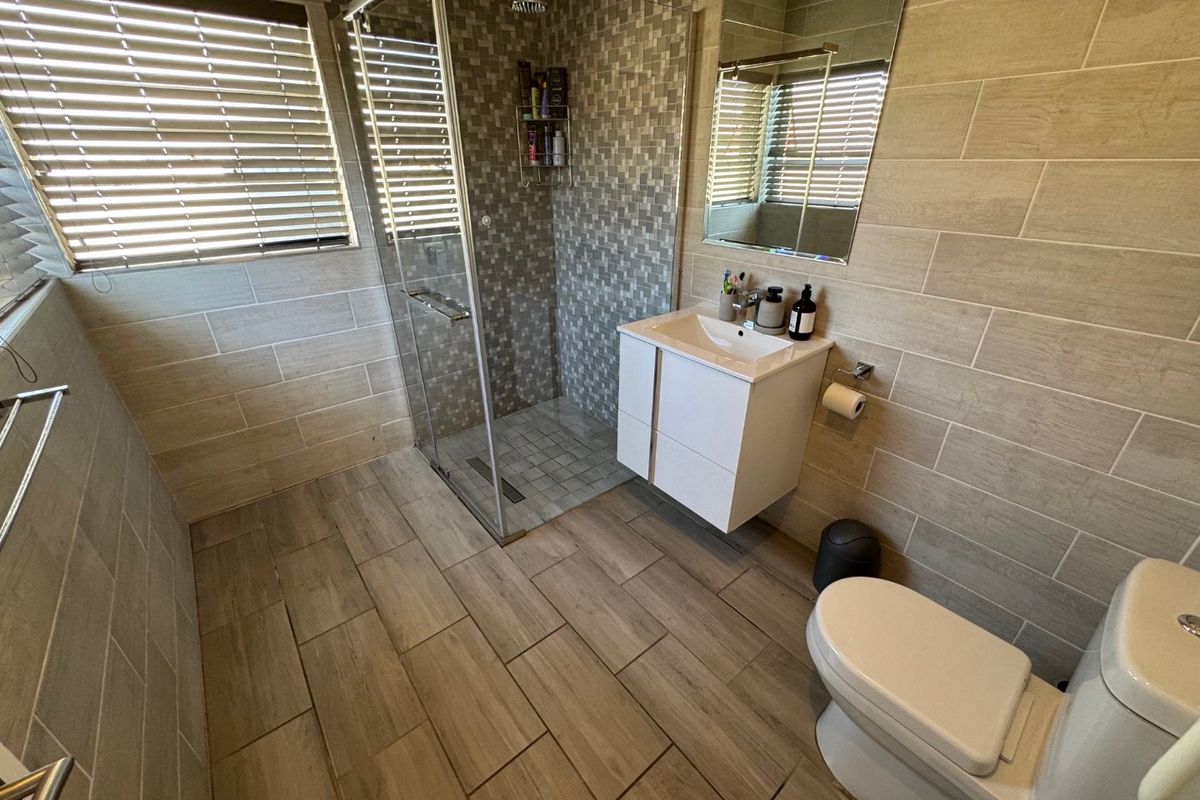 Modern bathroom featuring a glass-enclosed shower with mosaic tiling, a wall-mounted vanity, and neutral wood-look floor tiles.