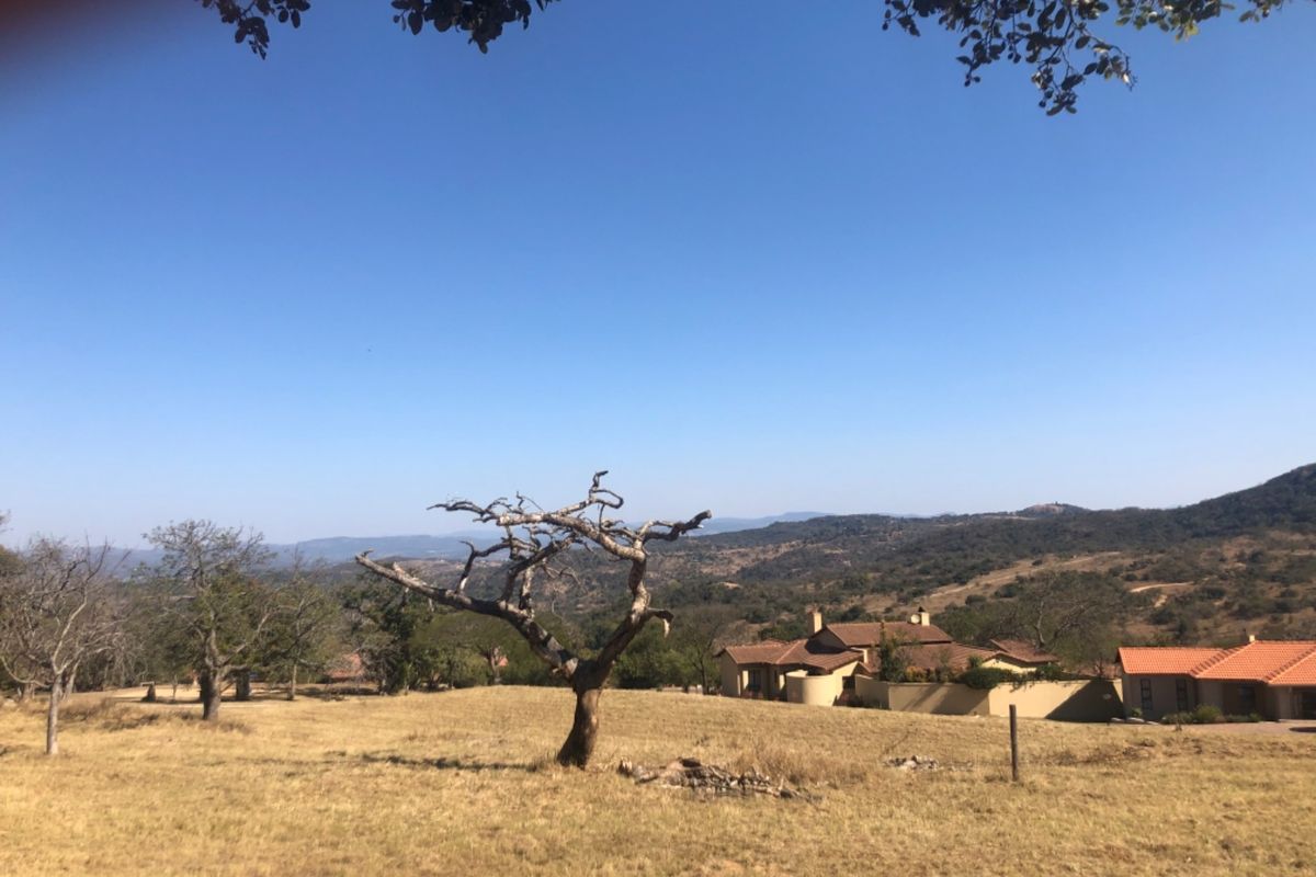 A scenic view of the expansive residential land featuring natural vegetation and distant housing structures under a clear blue sky.