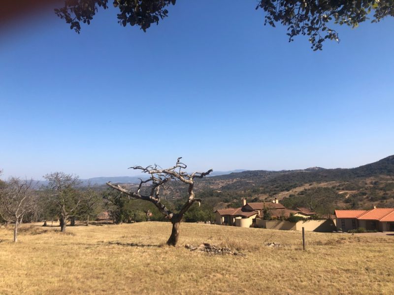 A scenic view of the expansive residential land featuring natural vegetation and distant housing structures under a clear blue sky.