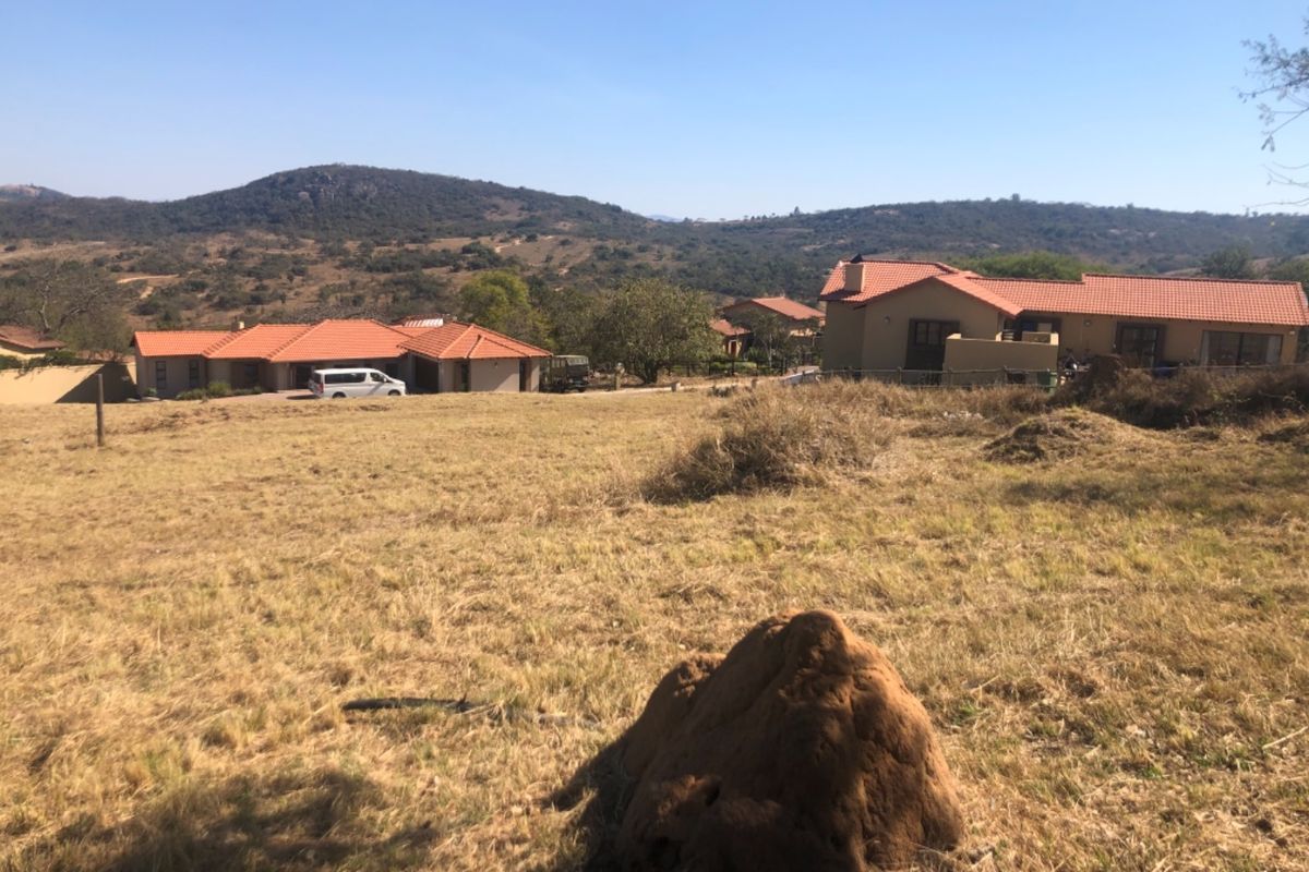 A view of an undeveloped residential plot with surrounding houses and scenic mountain landscape in the background.