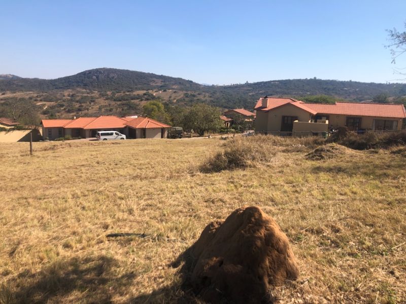 A view of an undeveloped residential plot with surrounding houses and scenic mountain landscape in the background.