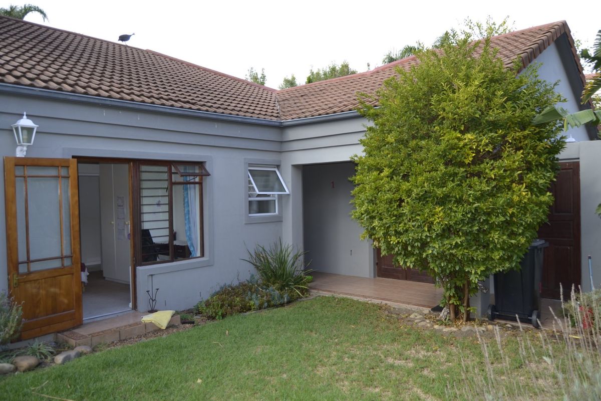 A view of the rear exterior featuring a tiled roof, timber door and window frames, and a small paved patio area adjacent to the garden.