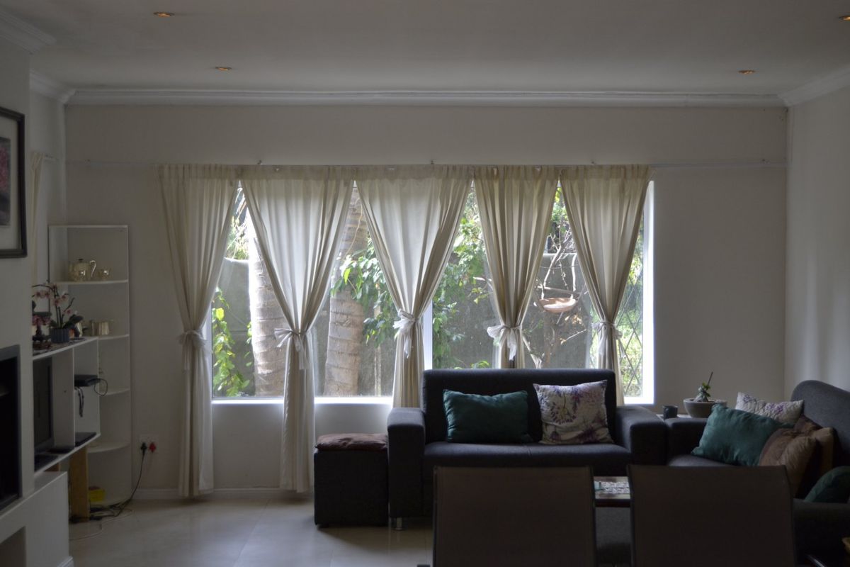 A living room featuring large windows with garden views, recessed downlighting, and neutral tiled flooring, offering a bright and comfortable space.