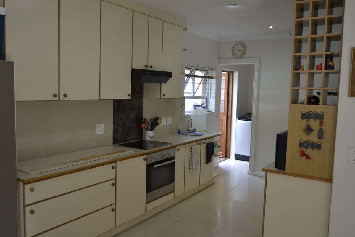 A functional kitchen featuring cream cabinetry, integrated oven and hob, tiled flooring, and a convenient adjacent laundry area.