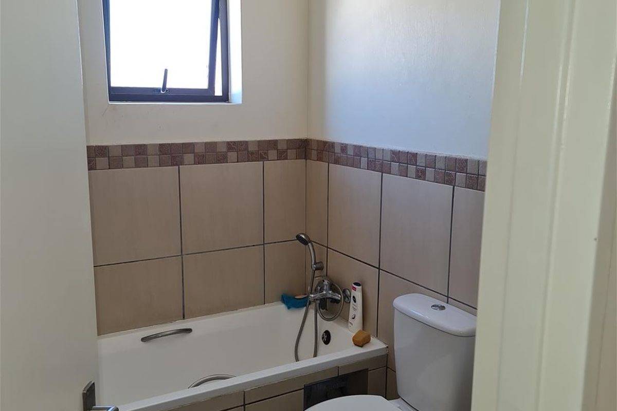 A compact bathroom featuring a bathtub, toilet, and neutral wall and floor tiling with a small window for natural light.