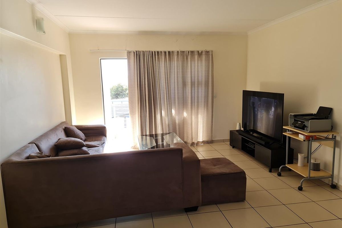 A functional living room featuring neutral tiled flooring and a sliding glass door providing access to an outdoor area.