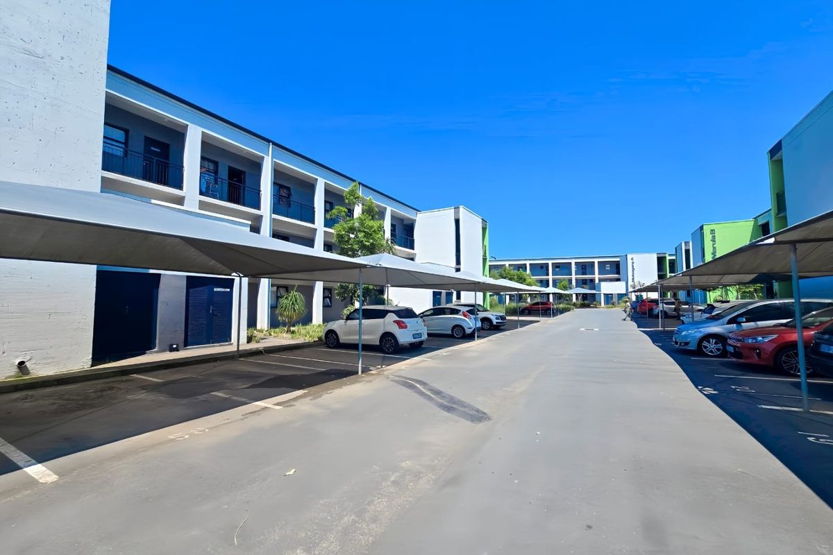Exterior view of the apartment complex parking area featuring covered shade-net parking bays and multi-story residential building blocks.