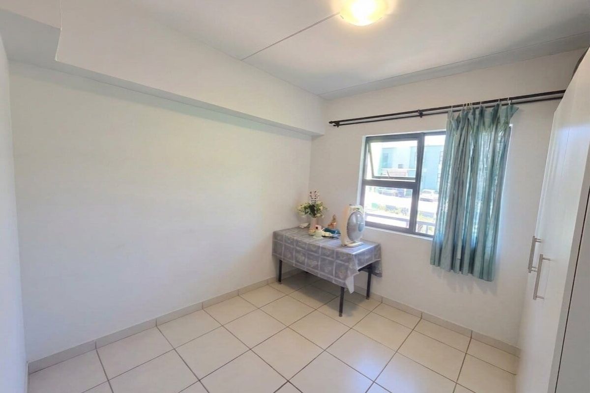 A bright, neutral bedroom featuring tiled flooring, a built-in wardrobe, and a window with curtain rails.
