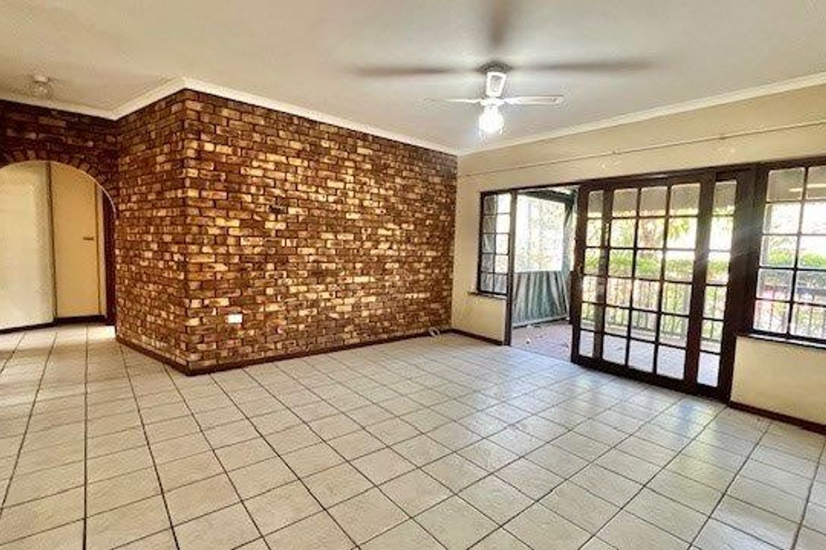 Spacious living area featuring a prominent face-brick accent wall, tiled flooring, and large sliding glass doors providing access to the patio.