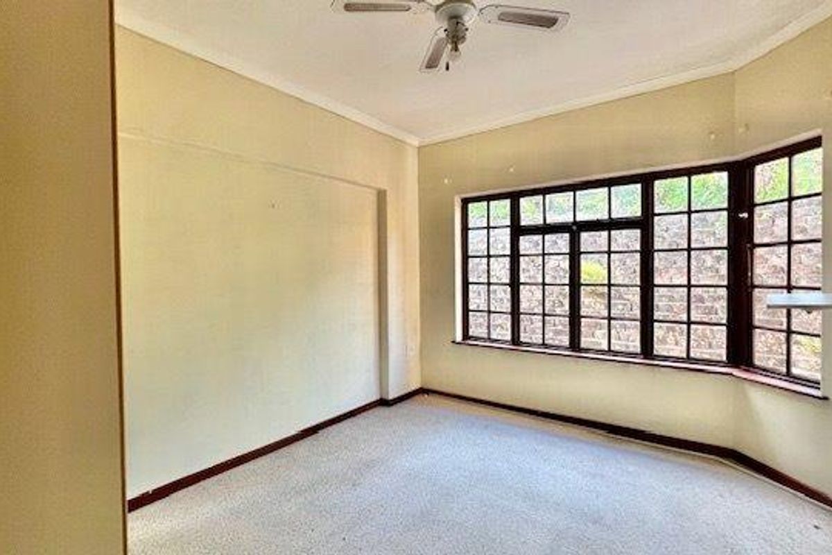 A vacant bedroom featuring a bay window, ceiling fan, and carpeted flooring, offering a blank canvas for renovation.