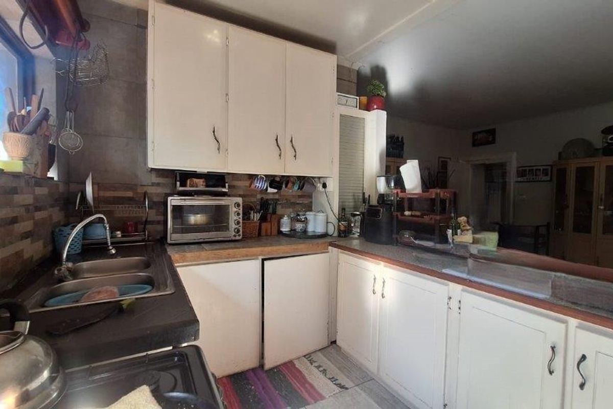 A functional kitchen featuring white cabinetry, tiled backsplash, and double bowl sink, offering potential for modernization through updated finishes and fixtures.