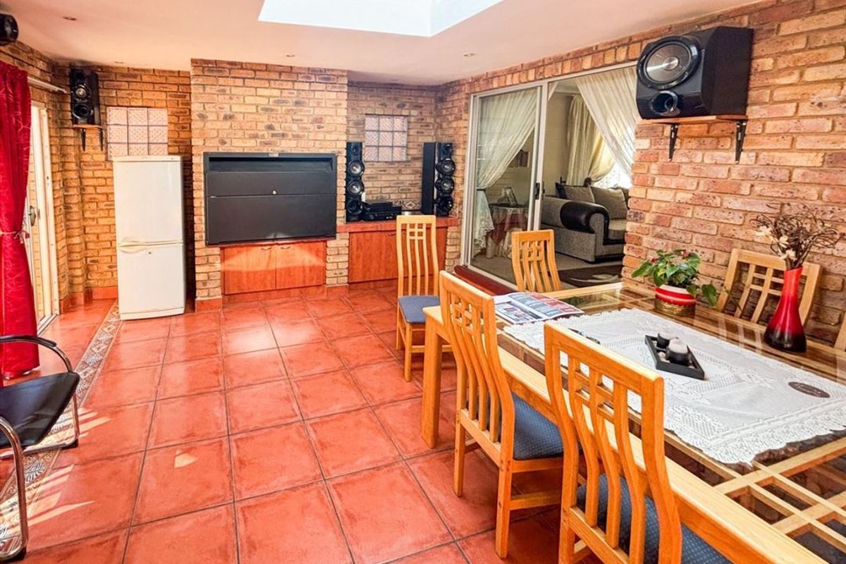 Enclosed patio area featuring exposed brick walls, a built-in braai, tiled flooring, and a large skylight, providing a versatile indoor-outdoor entertainment space.