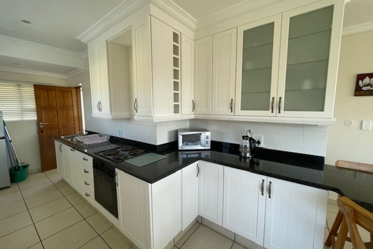 A functional kitchen featuring white cabinetry, dark granite countertops, an integrated electric hob and oven, and neutral tiled flooring.