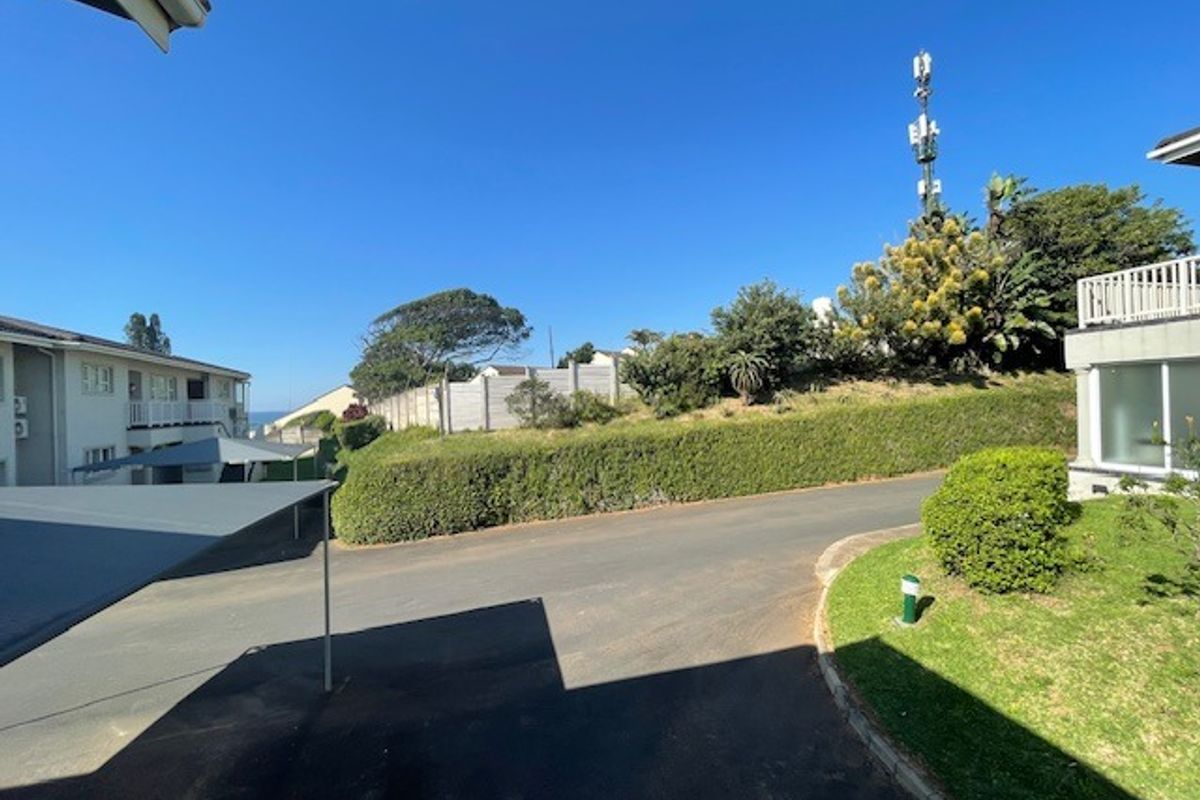An exterior view of the apartment complex grounds featuring paved driveway areas, landscaped garden beds, and a concrete boundary wall.