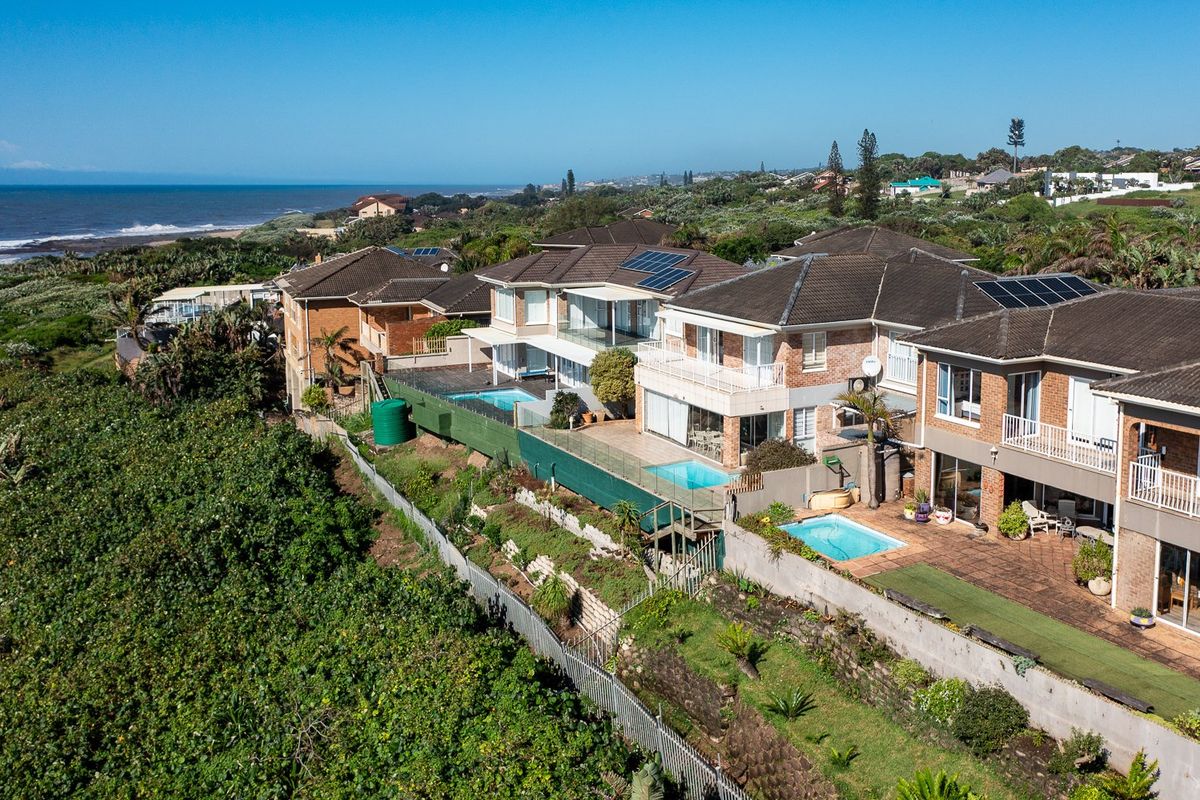 Aerial view of a coastal residential complex featuring multiple homes with tiled roofs, solar panels, private swimming pools, and ocean views.