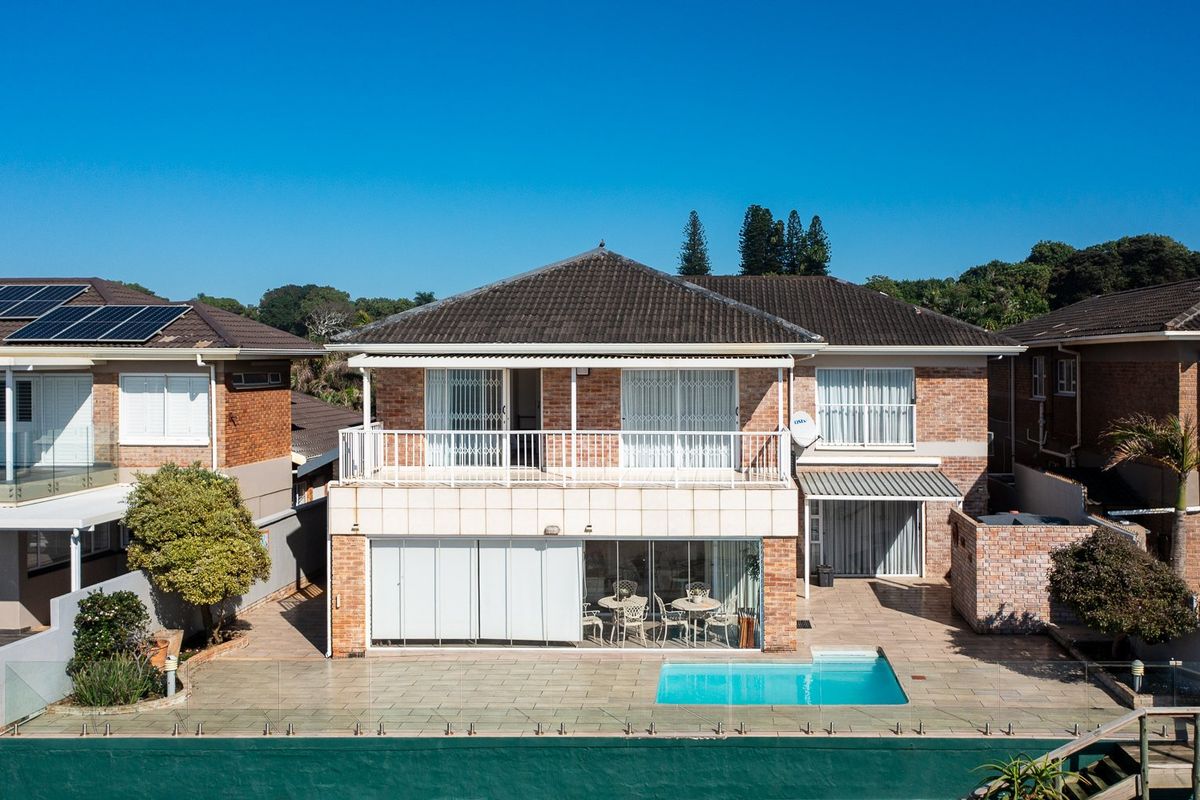 Rear view of a two-story brick house featuring a swimming pool, tiled patio area, upper-level balcony, and retractable awnings.