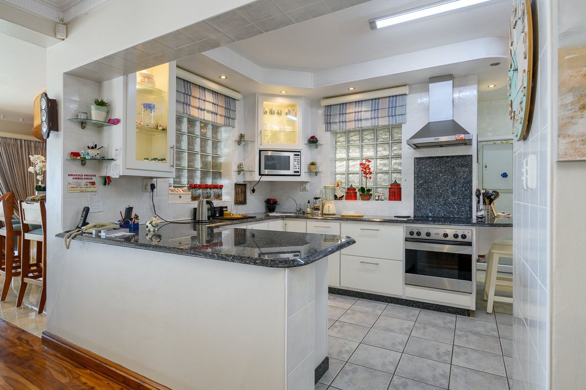 A functional kitchen featuring granite countertops, built-in oven with extractor fan, glass block windows, and tiled flooring, offering a practical layout for daily use.