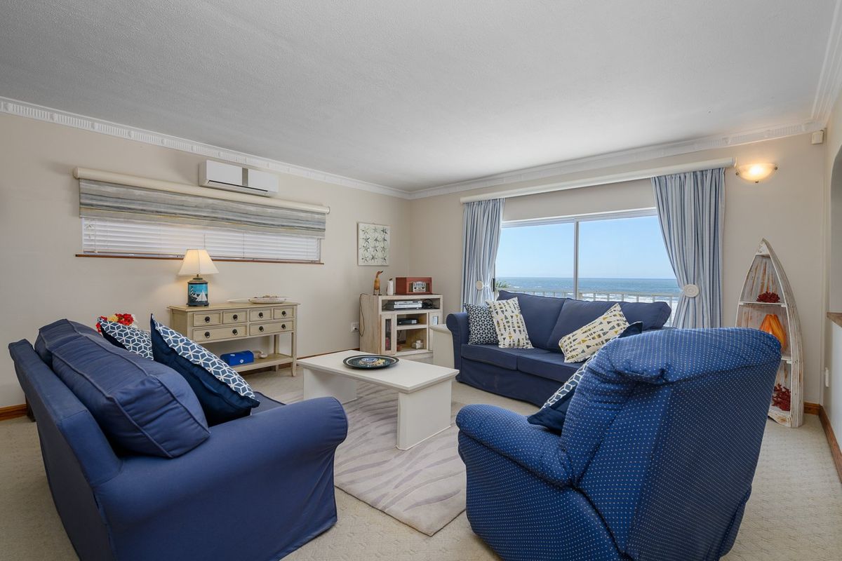 A comfortable living room featuring crown molding, a split-system air conditioner, and large sliding glass doors offering scenic ocean views.