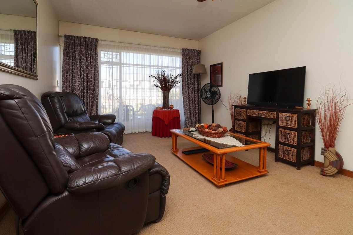 A comfortable living room featuring carpeted flooring and large windows with curtains, providing natural light and access to the outdoor area.