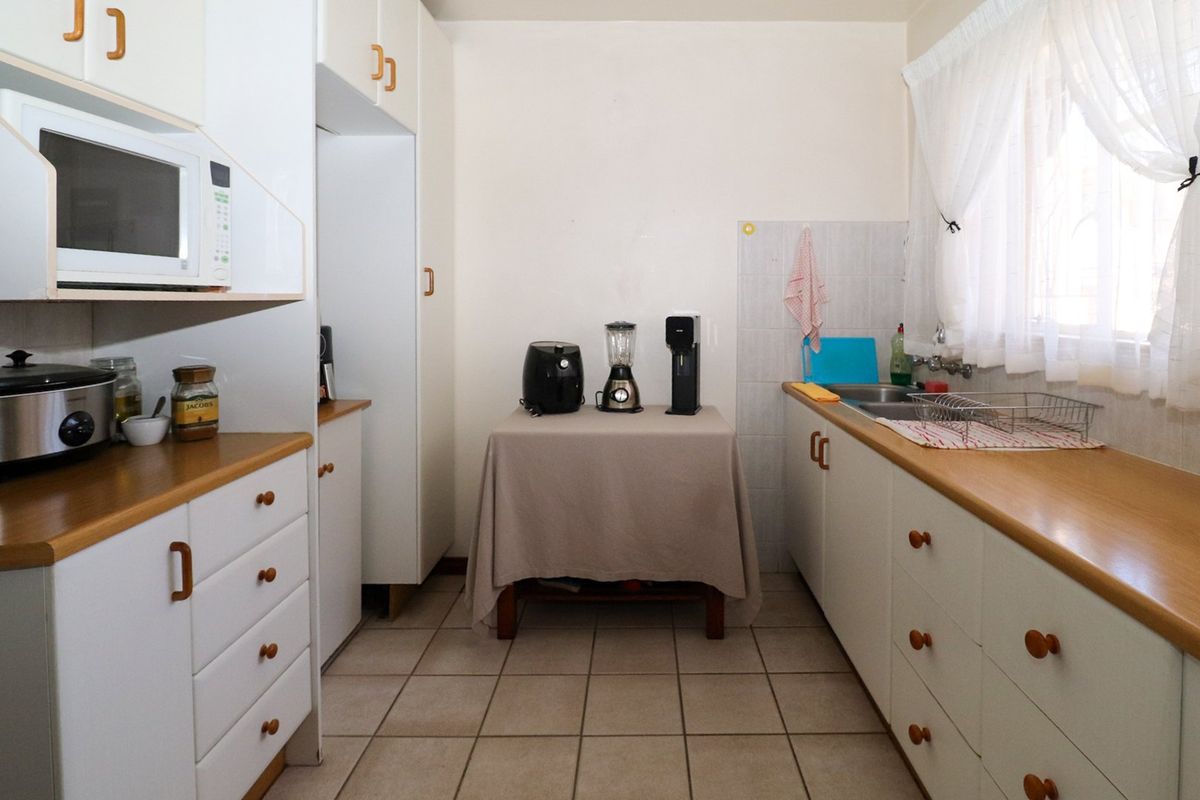 A functional galley-style kitchen featuring white cabinetry, wood-look laminate countertops, a double basin sink, and tiled flooring.