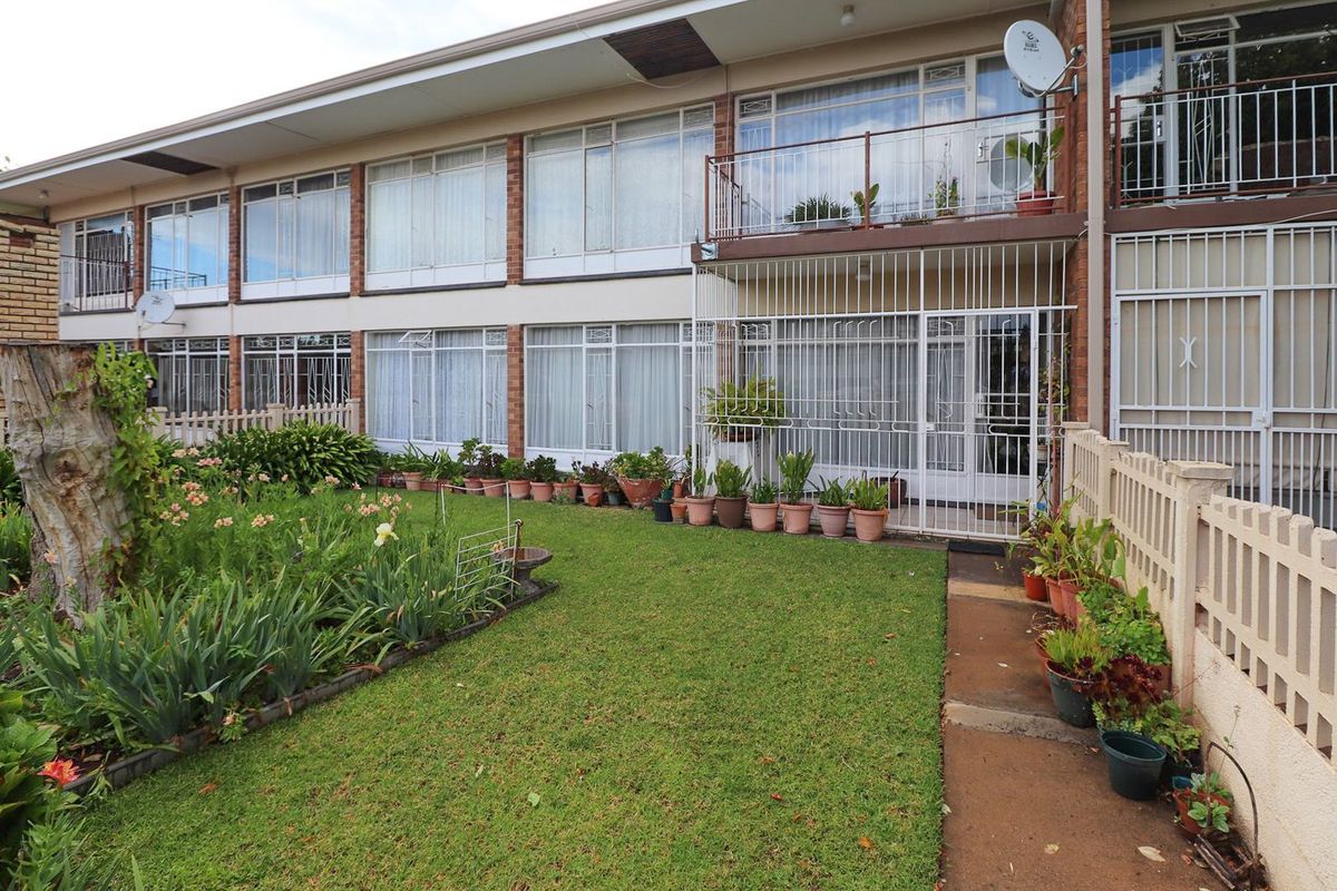 Rear view of a multi-story apartment building featuring ground floor garden access, security gates, and upper-level balconies with large windows.
