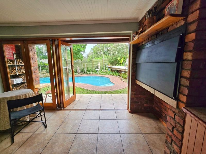 Covered patio area featuring a built-in braai, tiled flooring, and bi-fold doors opening directly onto a swimming pool and garden.