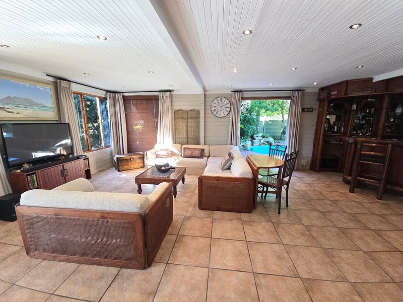 Spacious living area featuring tiled flooring, a timber-clad ceiling with recessed lighting, and a built-in bar, with direct access to the outdoor pool area.