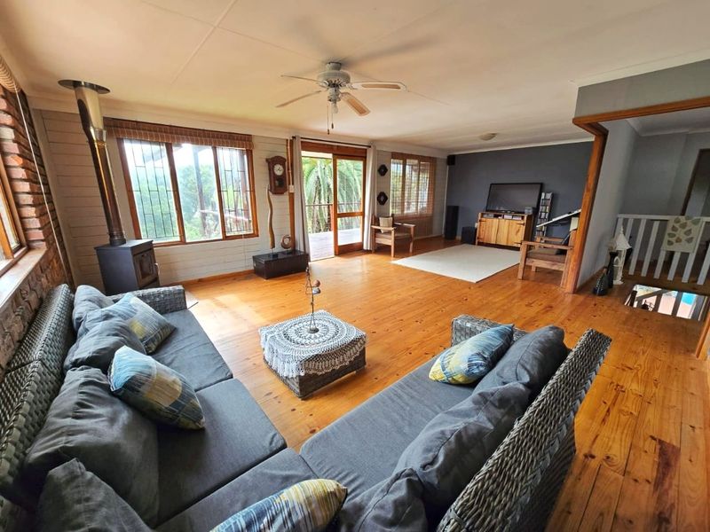 Spacious living room featuring warm timber flooring, a wood-burning stove, exposed brick accents, and direct access to an outdoor deck through sliding glass doors.