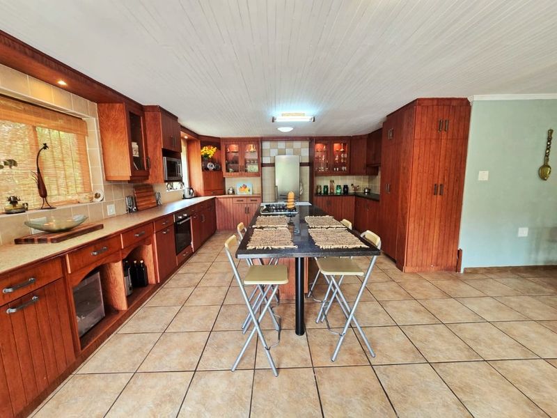 Spacious kitchen featuring extensive wooden cabinetry, a central island with seating, tiled flooring, and a classic tongue and groove ceiling.
