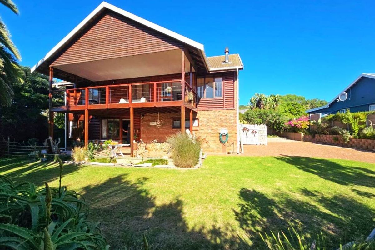 Rear view of a two-story house featuring timber cladding, a spacious raised wooden deck, a paved patio area, and a well-maintained garden.