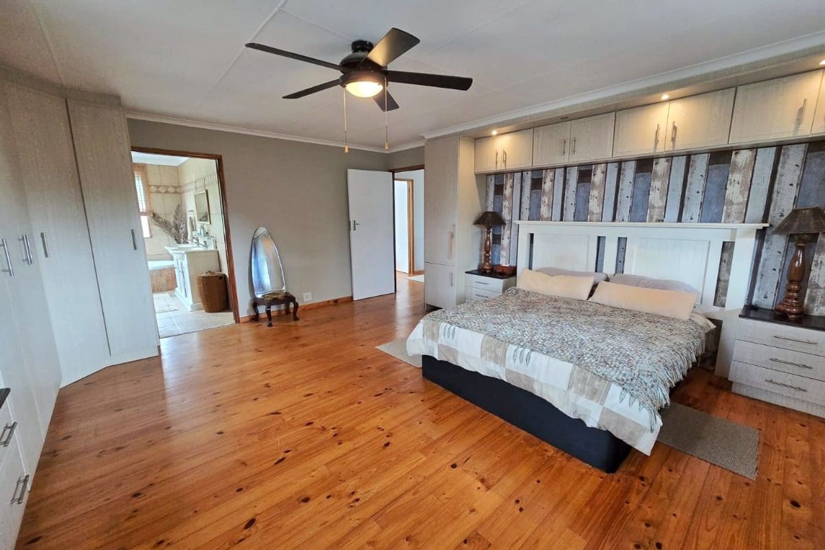 Spacious bedroom featuring polished wooden flooring, extensive built-in cabinetry, a ceiling fan, and direct access to an en-suite bathroom.
