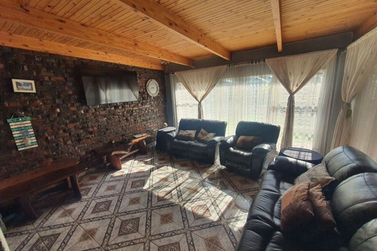A cozy living room featuring an exposed brick feature wall, rustic timber beam ceiling, and patterned ceramic floor tiles with access to the garden.
