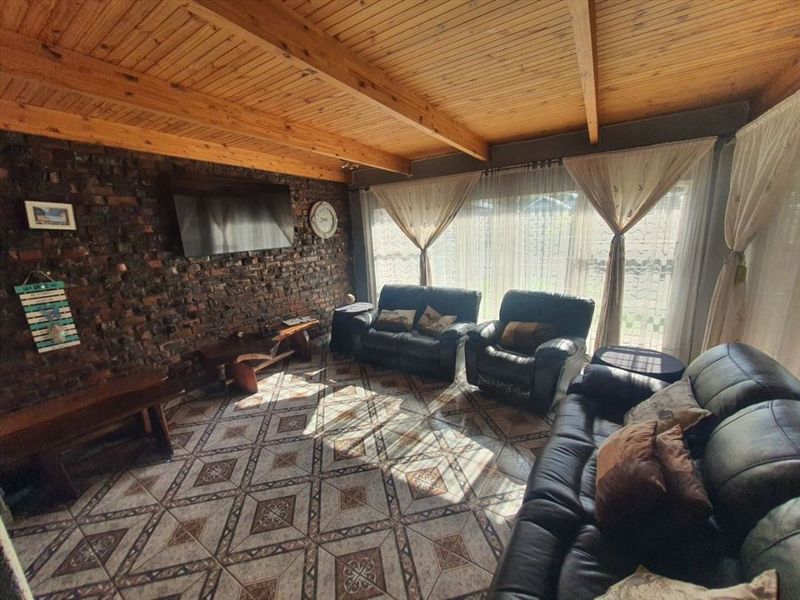 A cozy living room featuring an exposed brick feature wall, rustic timber beam ceiling, and patterned ceramic floor tiles with access to the garden.