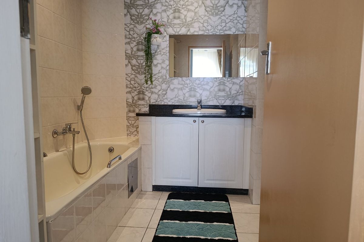 A functional bathroom featuring a built-in vanity with granite countertop, a bathtub with handheld shower mixer, and decorative wall tiling.