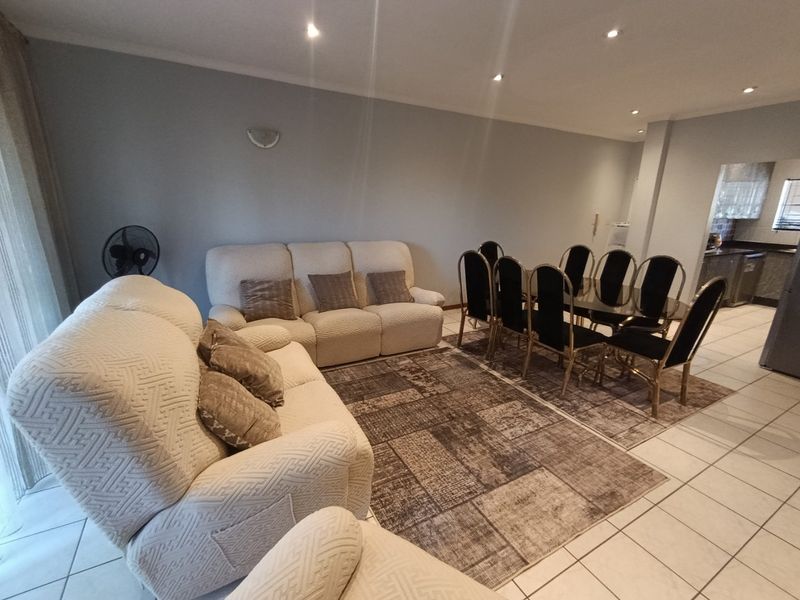 Open-plan living and dining area featuring neutral wall tones, ceramic floor tiles, and recessed downlighting, providing a functional and connected living space.