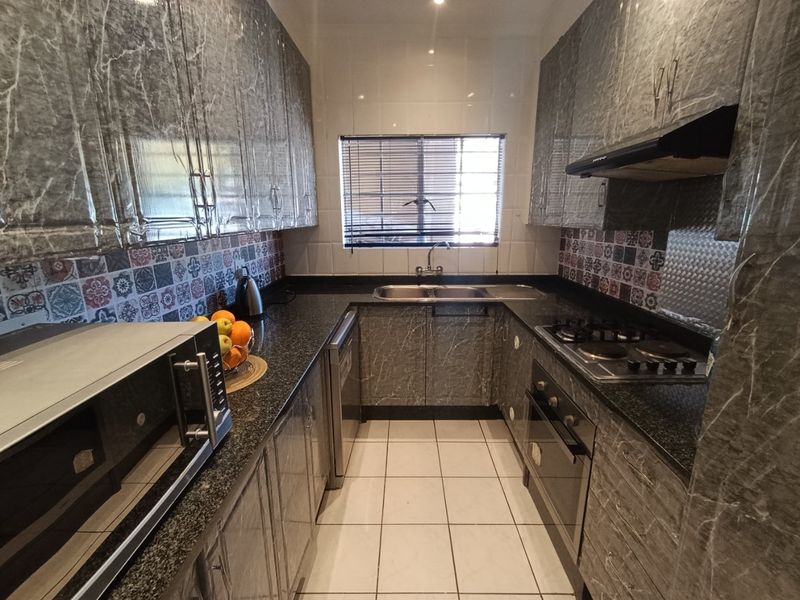 A compact galley-style kitchen featuring marble-effect cabinetry, granite countertops, a built-in oven with gas hob, and a tiled backsplash.