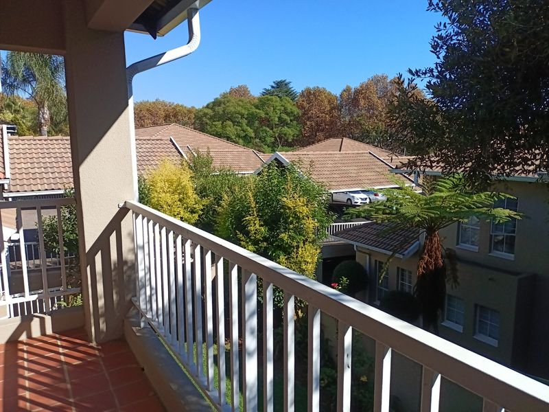 A covered balcony featuring tiled flooring and a white metal balustrade, overlooking the surrounding residential complex and mature trees.